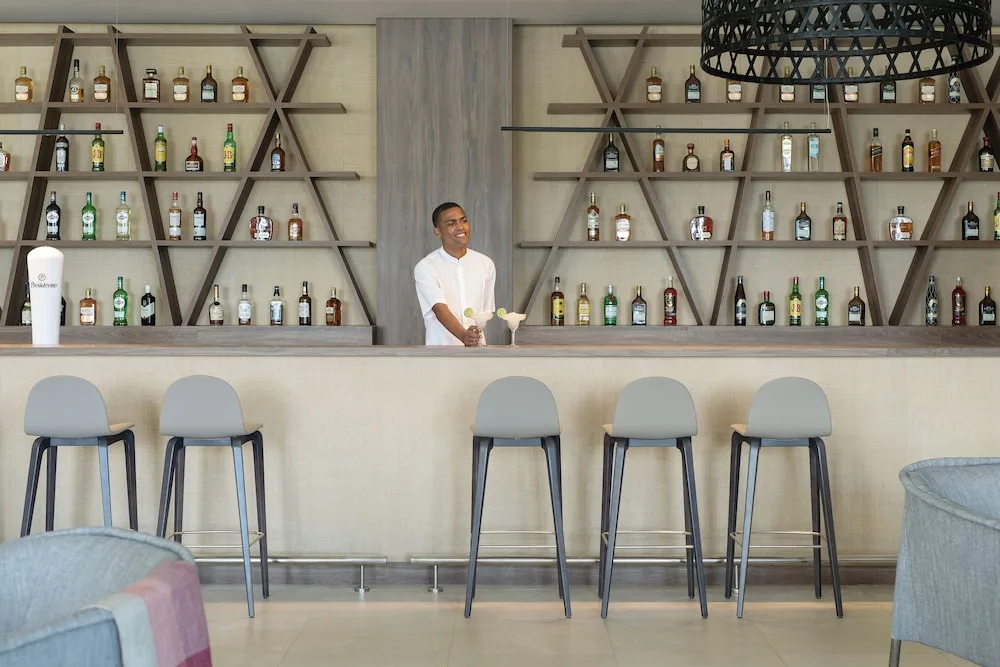 Lobby bar with geometric bottle shelves and stools at Excellence Punta Cana.