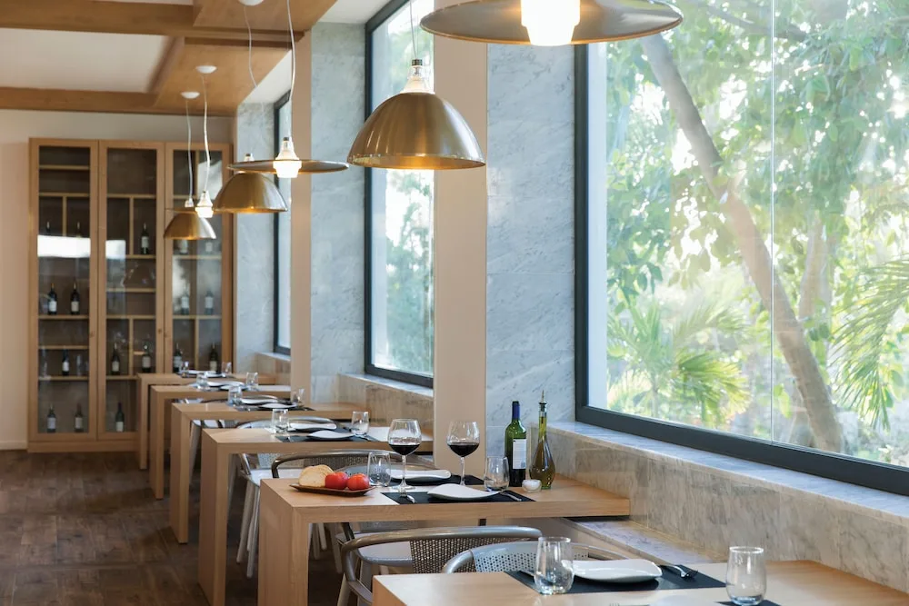 Window-side dining room with set tables and pendant lights at Excellence Punta Cana.