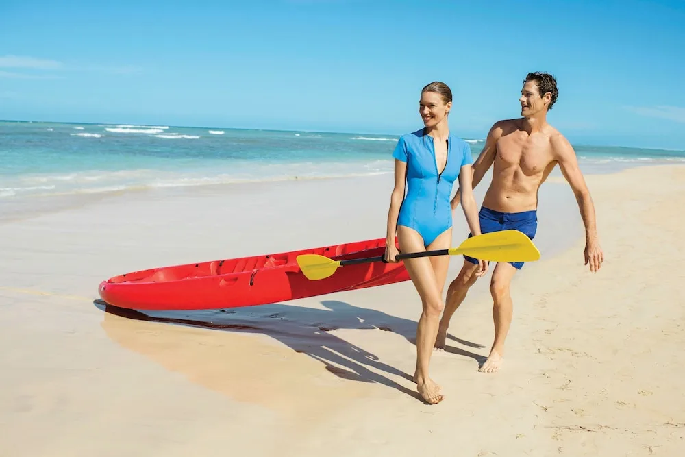 Couple walking with a red kayak on the beach at Excellence Riviera Cancun.