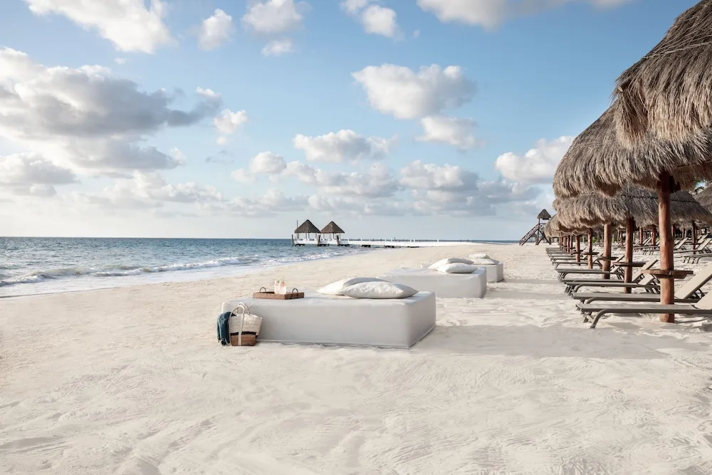 Beach loungers and thatched shade palapas on the sand at Excellence Riviera Cancun.