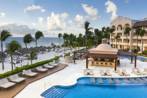 Beachfront pool, loungers, palms and ocean at Excellence Riviera Cancun.