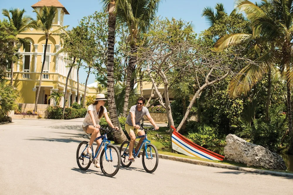 Guests riding blue bicycles along a palm-lined resort path at Excellence Riviera Cancun.