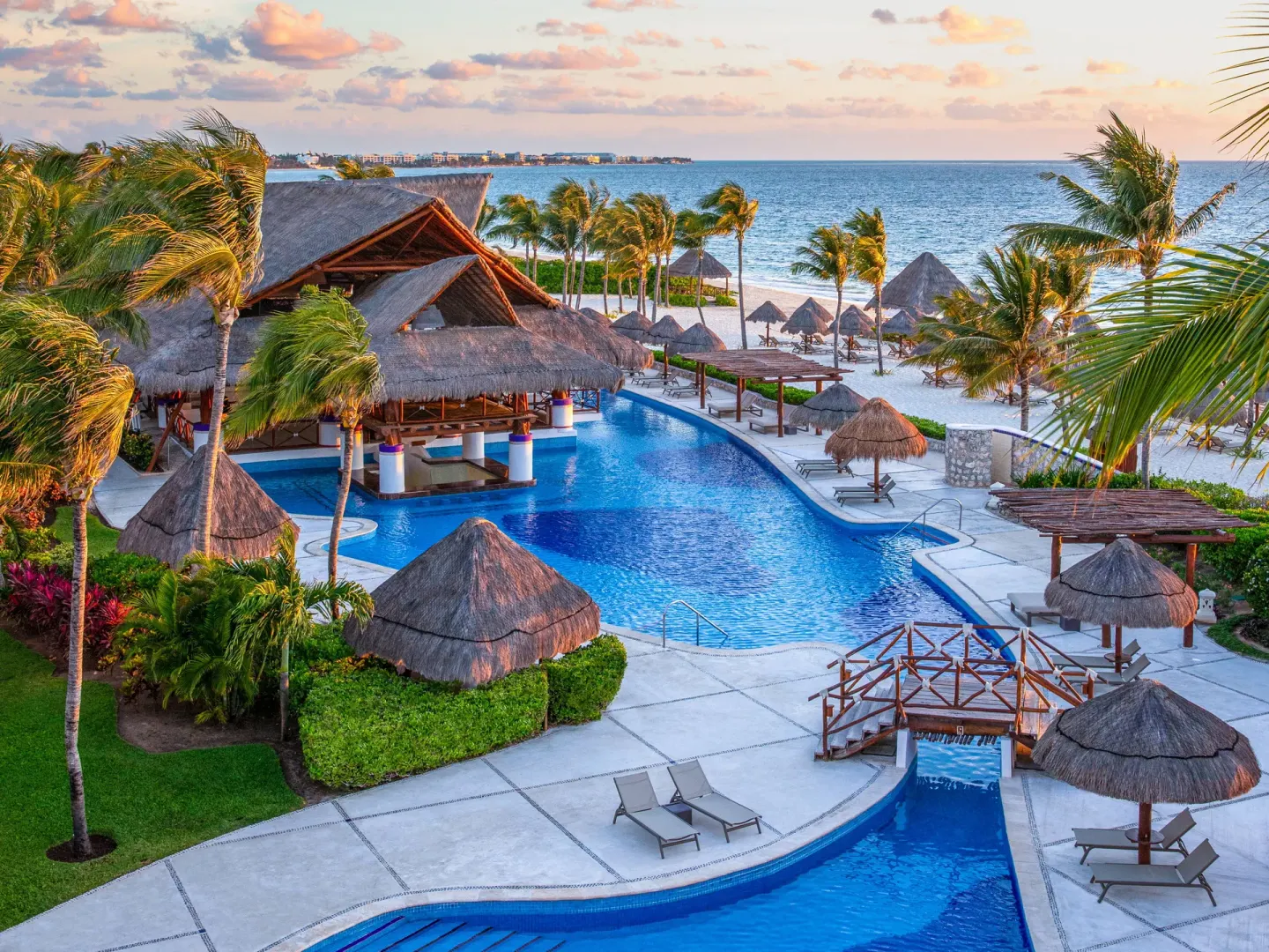 Oceanfront pool area with palapas at sunset at Excellence Riviera Cancun.