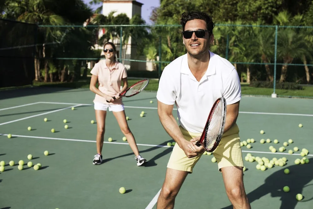 Guests playing tennis on an outdoor court at Excellence Riviera Cancun.