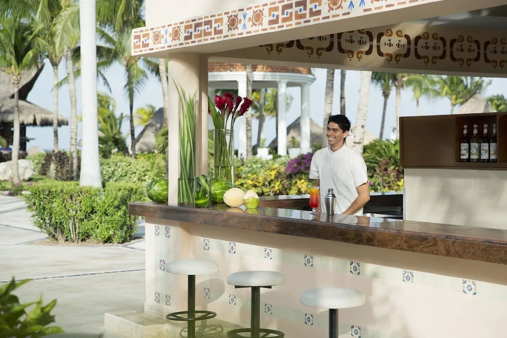 Outdoor resort bar with bartender and tropical landscaping at Excellence Riviera Cancun.