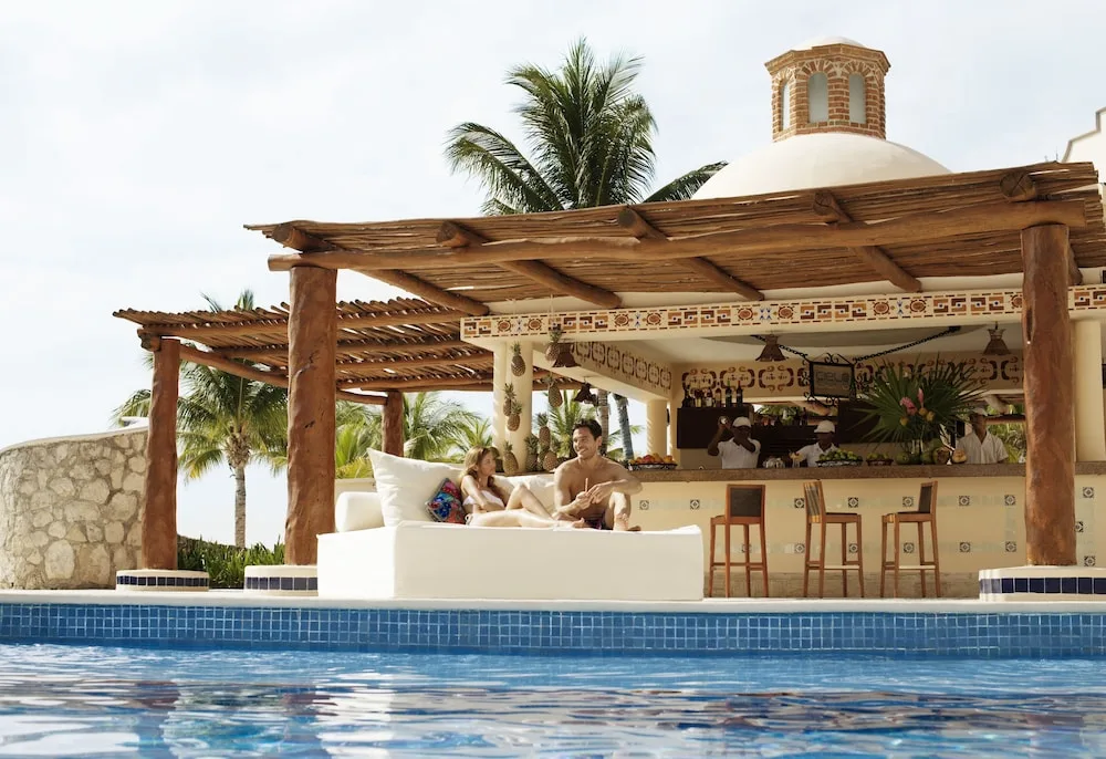 Swim-up pool bar with palapa roof and guests at Excellence Riviera Cancun.