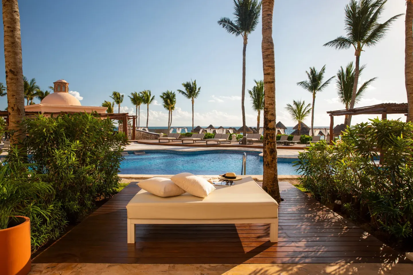 Swim-up terrace daybed by the pool at Excellence Riviera Cancun, with palms and ocean beyond.