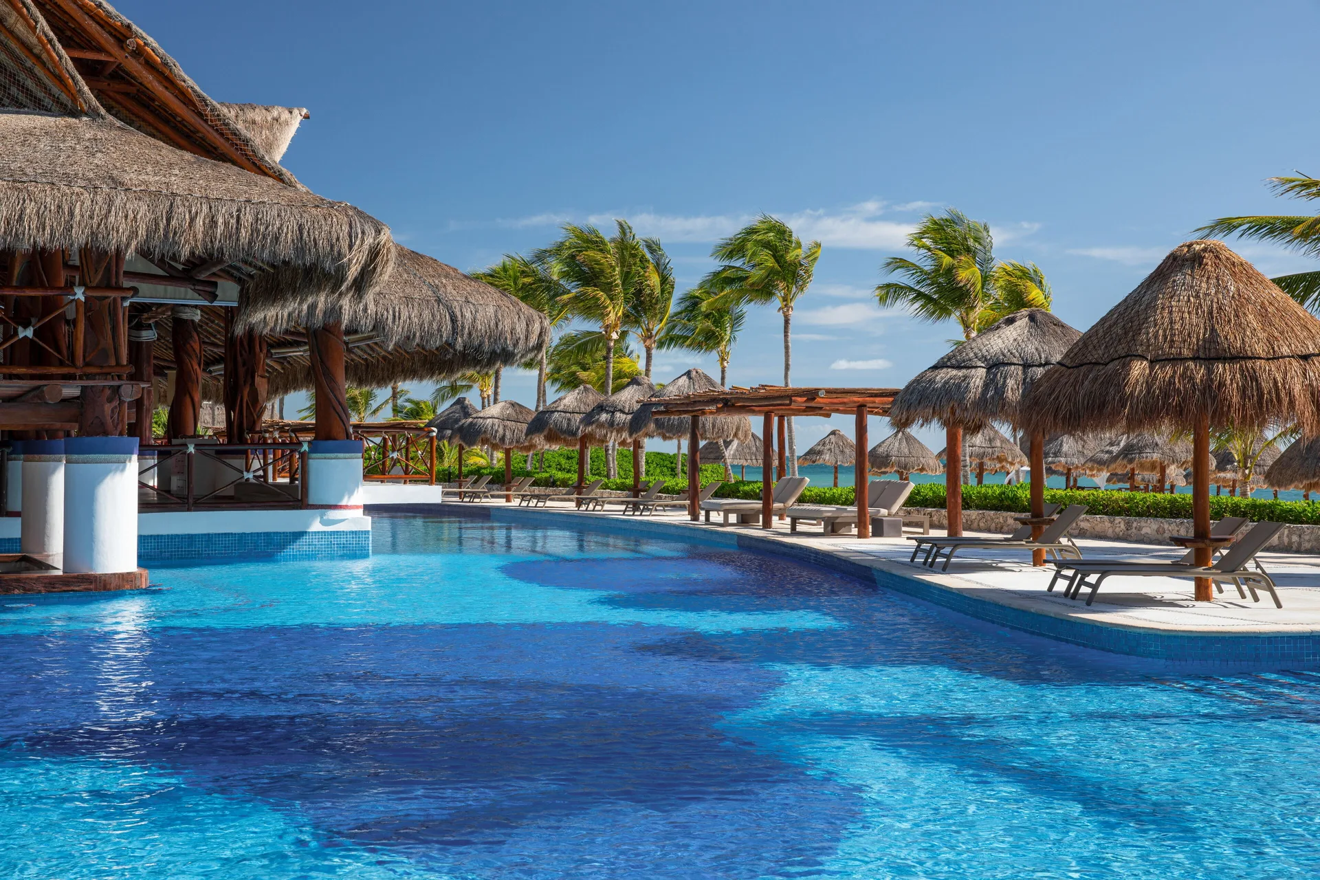 Pool with palapa shade structures and loungers at Excellence Riviera Cancun.