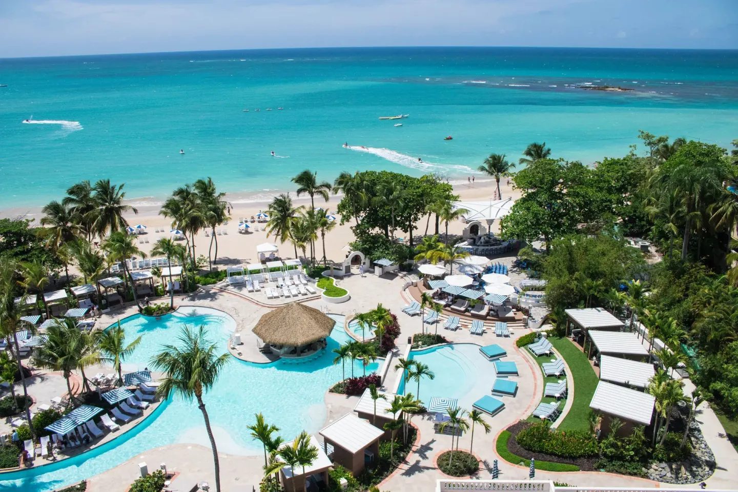 Aerial view of pools, palms, beach, and turquoise ocean at Fairmont El San Juan.