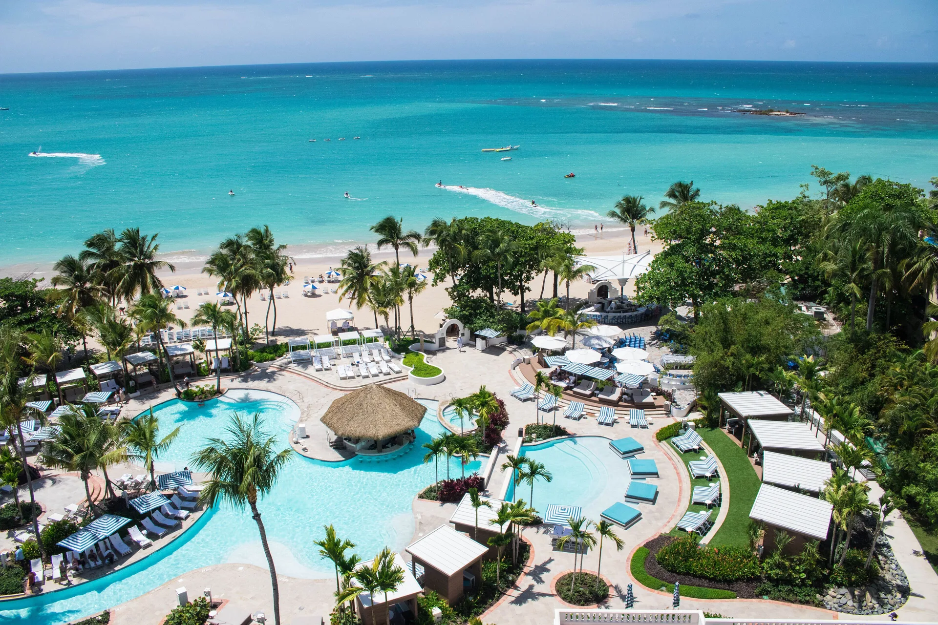 Aerial view of pools, palms, beach, and turquoise ocean at Fairmont El San Juan.