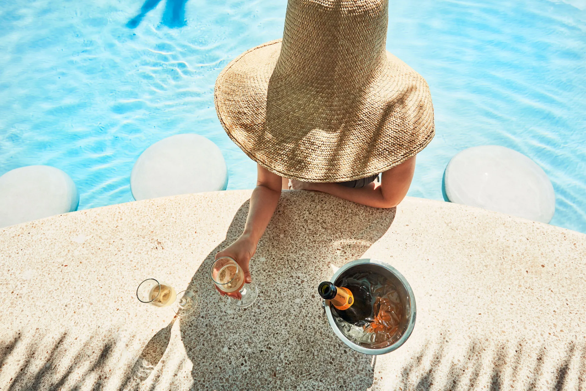 Guest in a wide sun hat holding a drink beside the pool at Fairmont El San Juan.