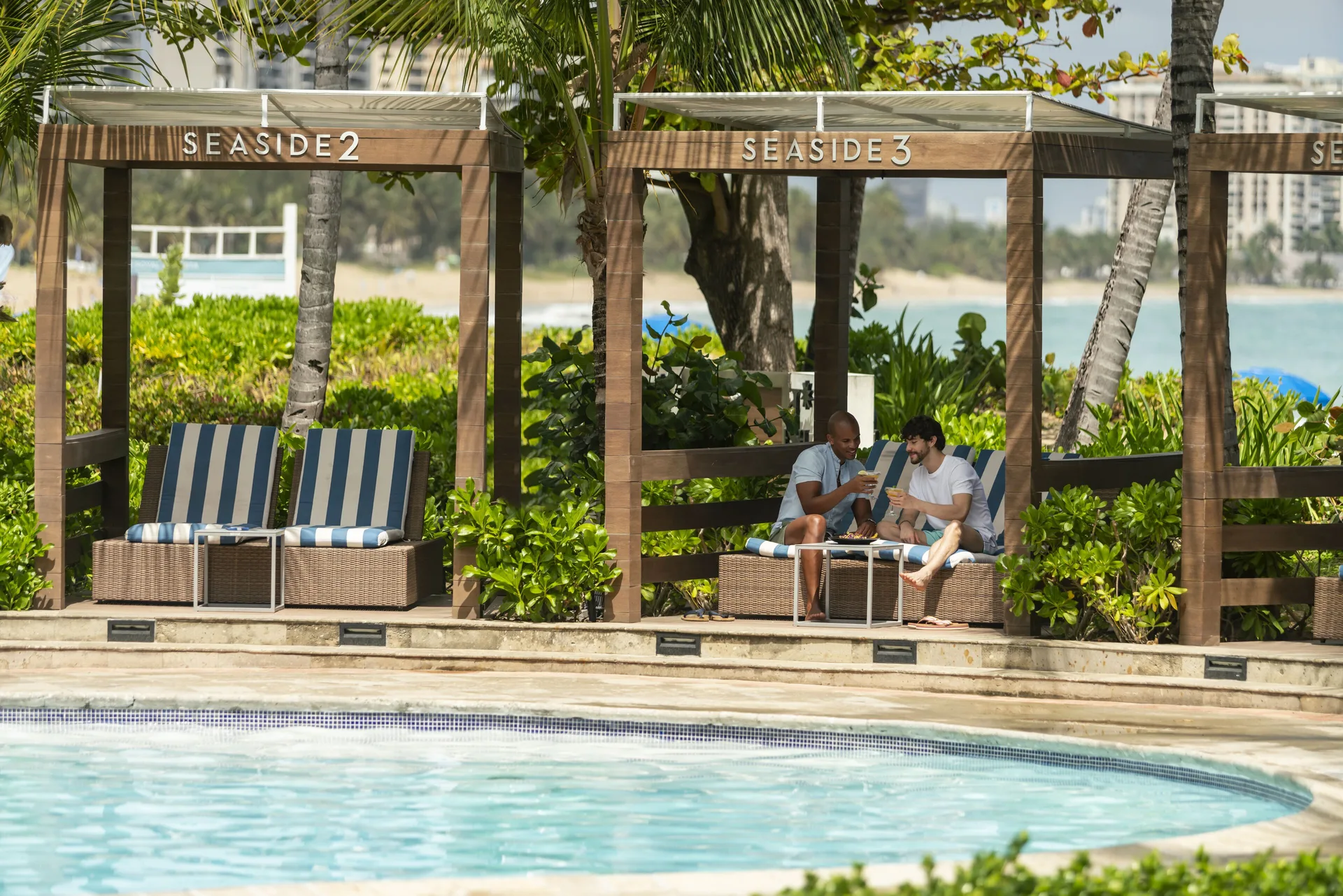 Seaside cabanas with striped seating face the pool at Fairmont El San Juan.