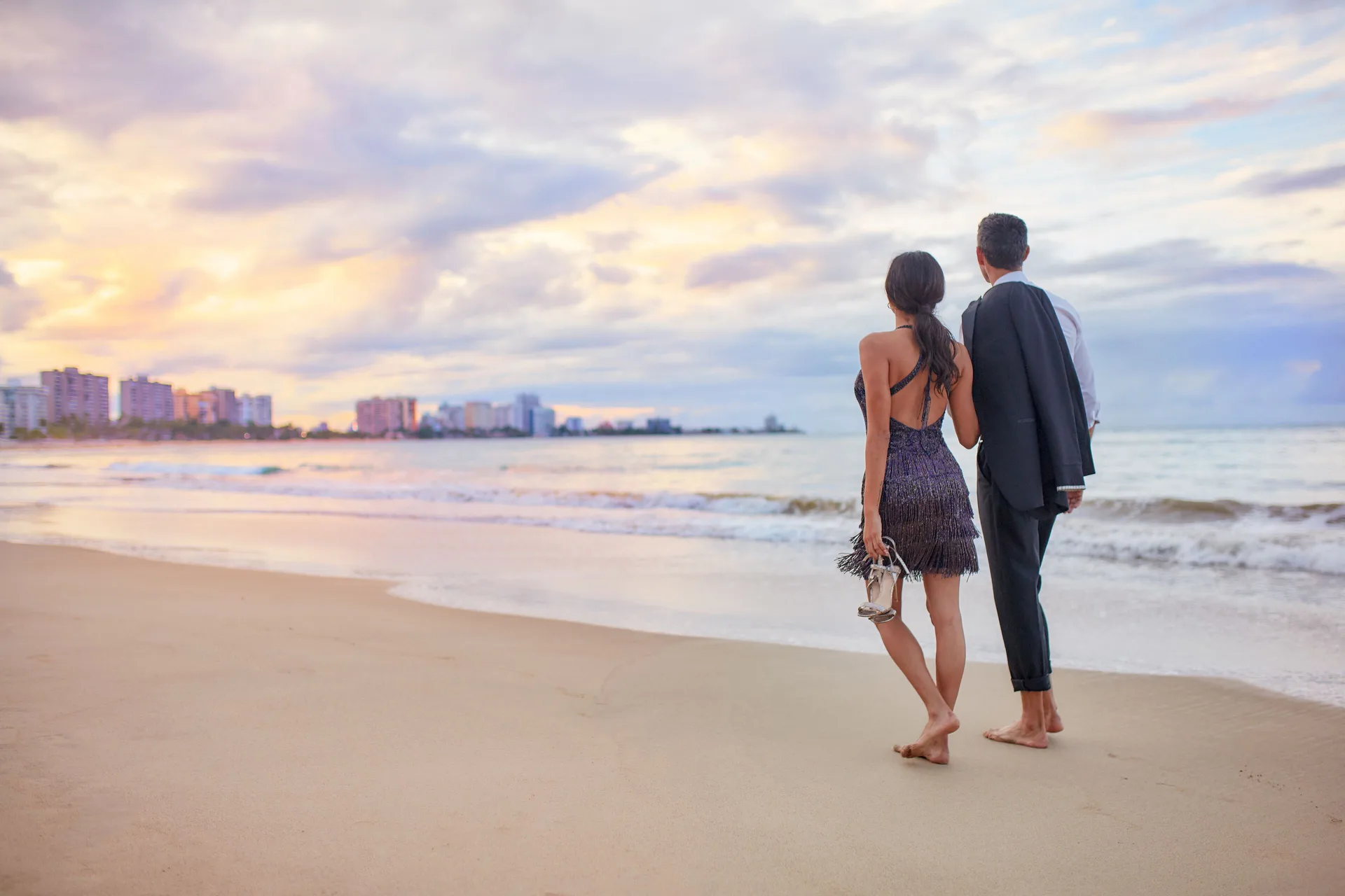 Couple walking barefoot on the beach at sunset near Fairmont El San Juan.