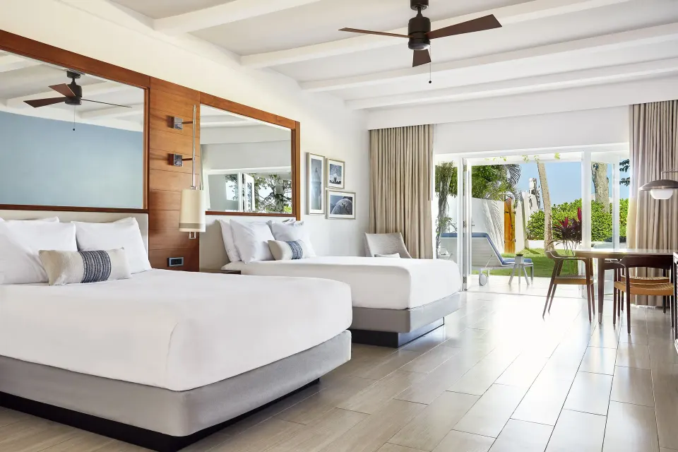 Two queen beds in a garden-view villa room at Fairmont El San Juan with a terrace beyond sliding doors.