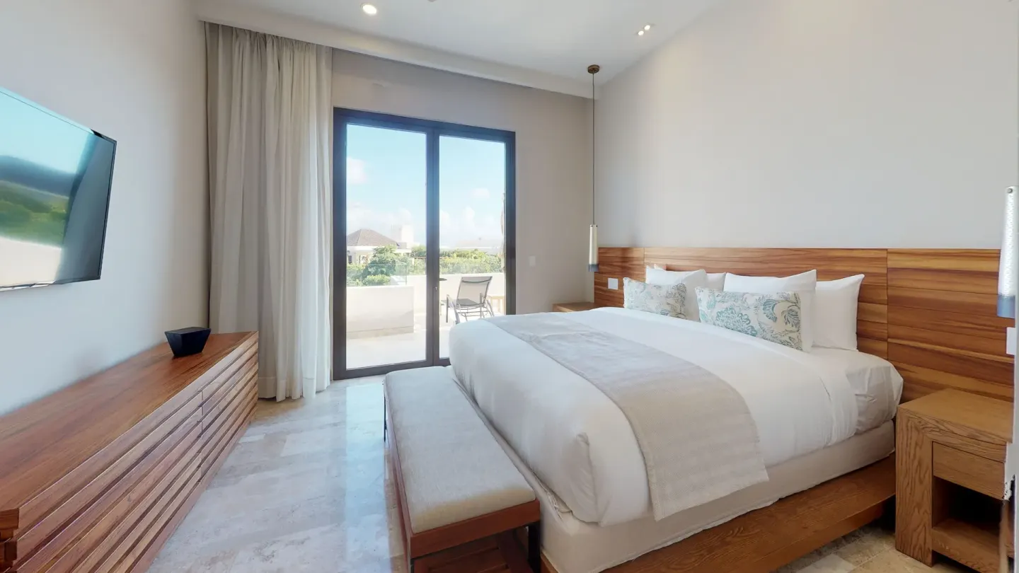 King-bed guest room with balcony doors and wall TV at Fairmont Heritage Place Mayakoba.