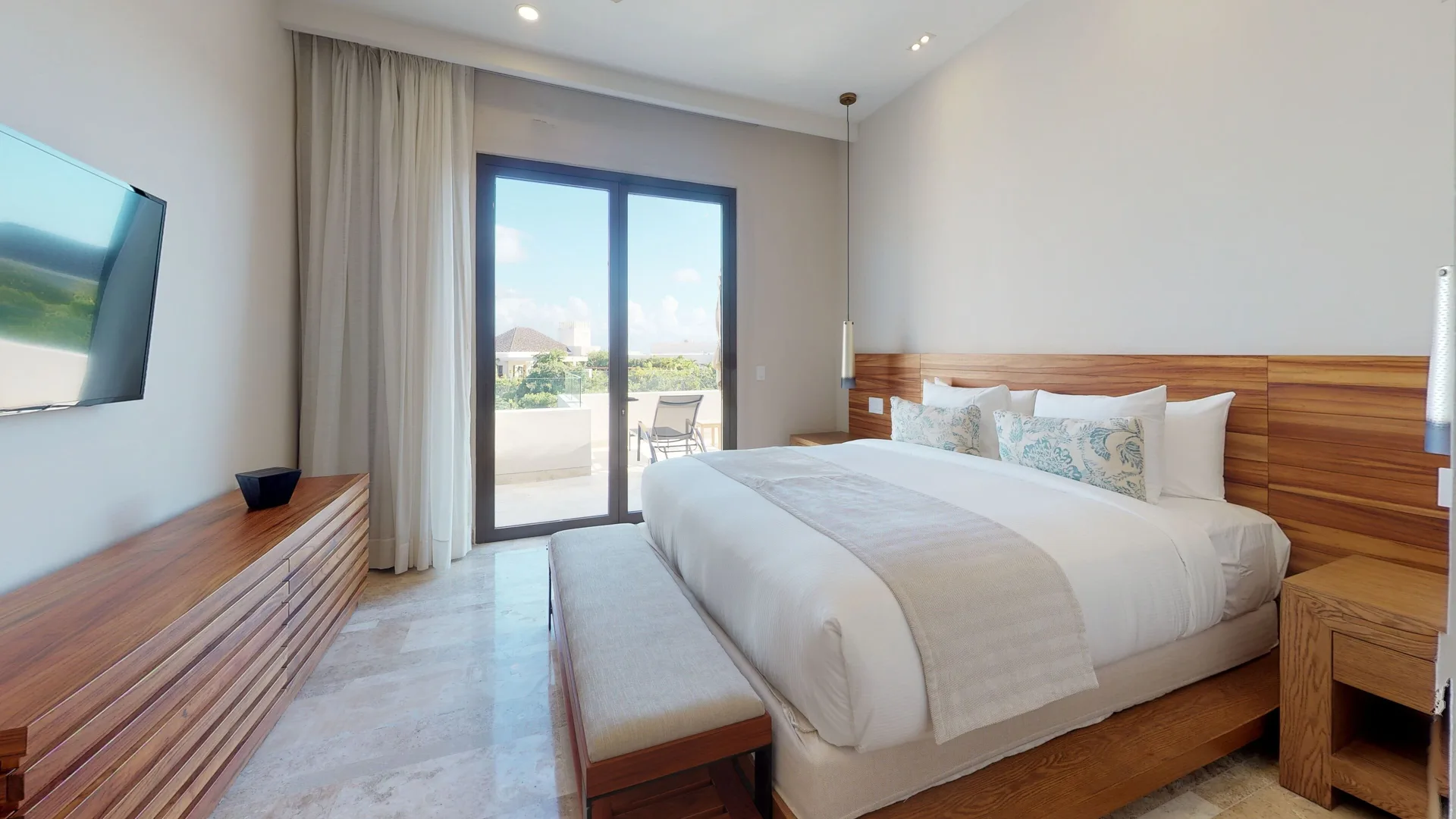King-bed guest room with balcony doors and wall TV at Fairmont Heritage Place Mayakoba.