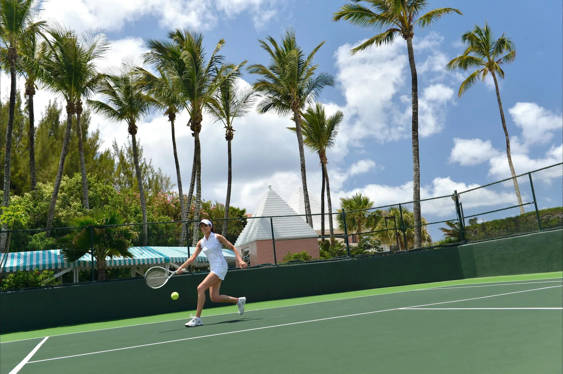 A tennis player returns a shot on a palm-lined court at Fairmont Heritage Place Mayakoba.