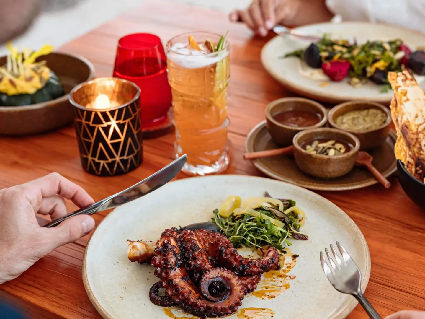 Grilled octopus, sauces, salad, and a cocktail on a table at Fairmont Heritage Place Mayakoba.