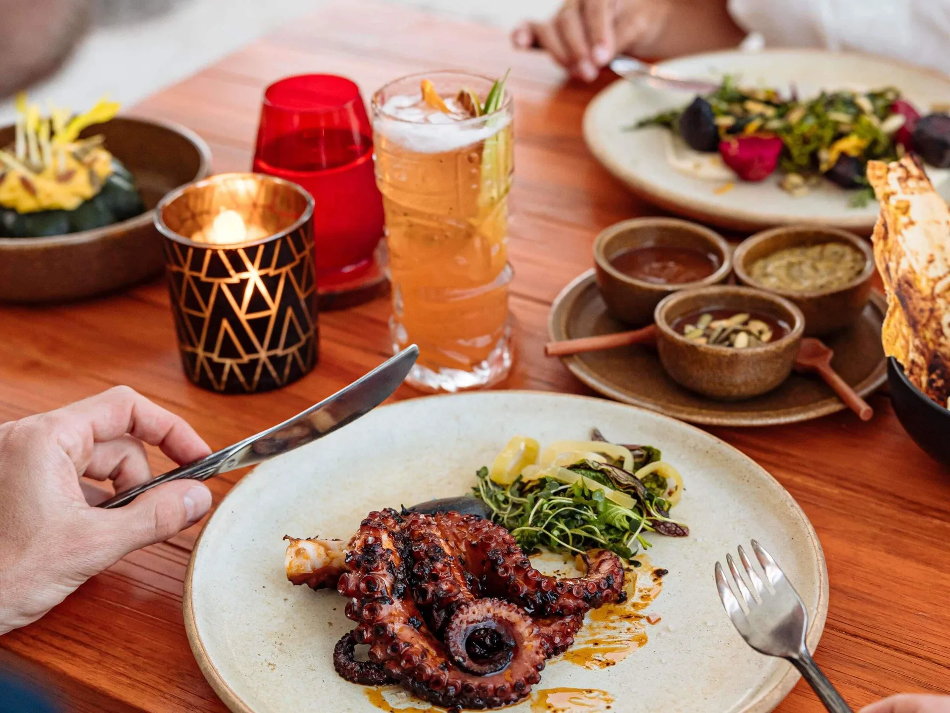 Grilled octopus, sauces, salad, and a cocktail on a table at Fairmont Heritage Place Mayakoba.