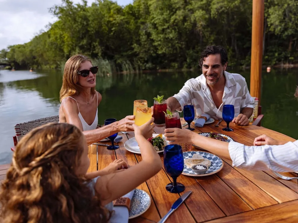 Guests raise colorful drinks at a waterfront table at Fairmont Heritage Place Mayakoba.