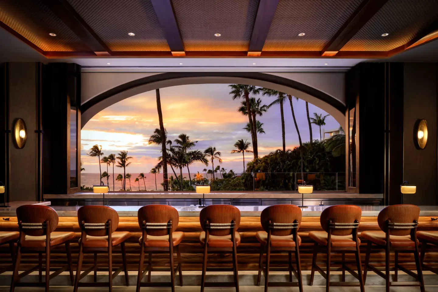 Bar seating frames a palm-lined sunset view at Fairmont Kea Lani Maui.