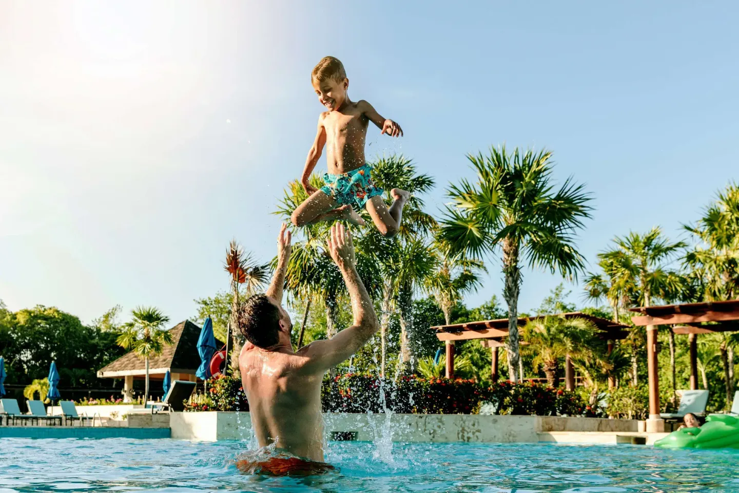 Adult tossing a child into the pool with palm trees behind them at Fairmont Mayakoba.
