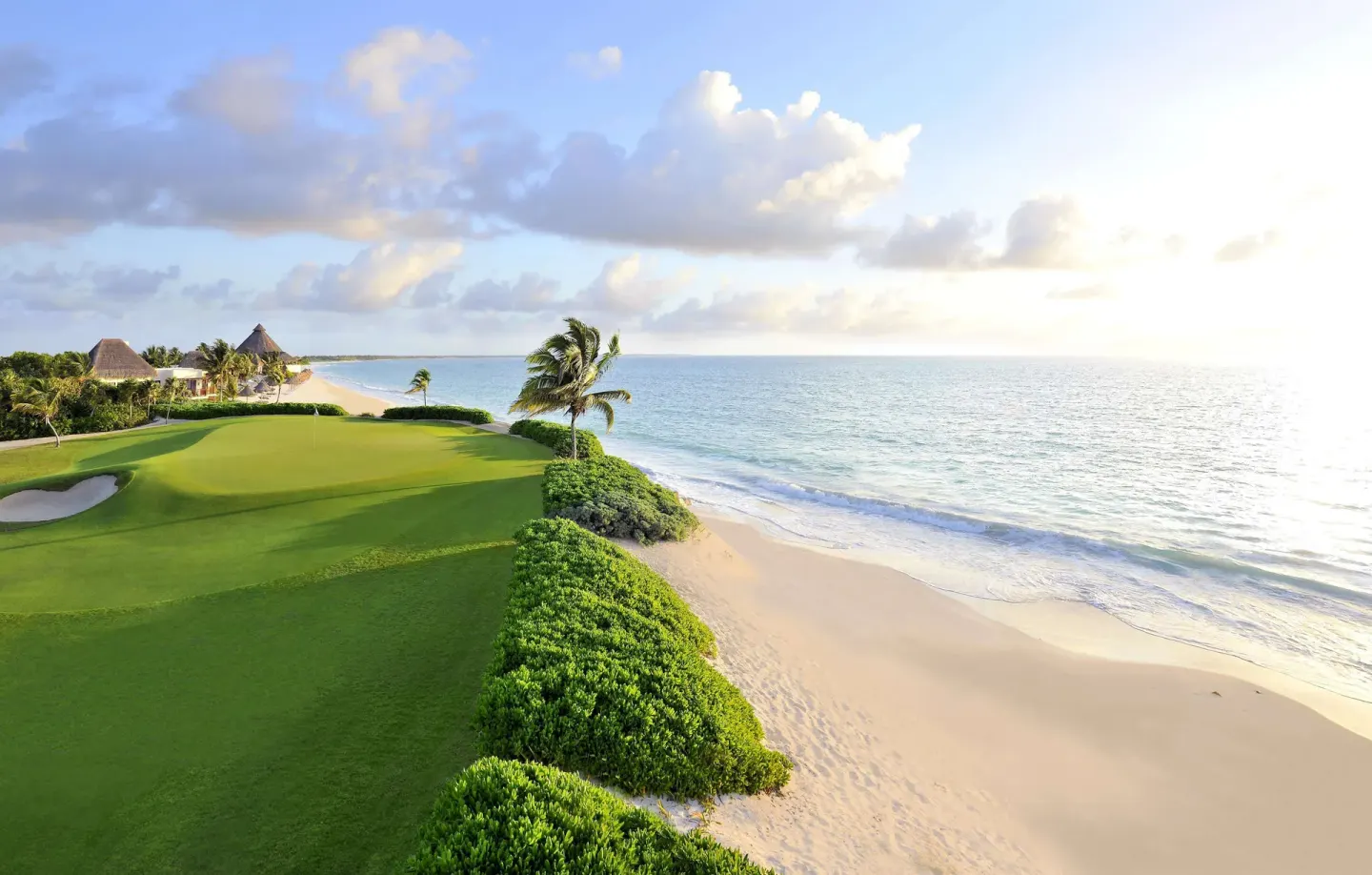Oceanfront golf green beside a sandy beach and palms at Fairmont Mayakoba.