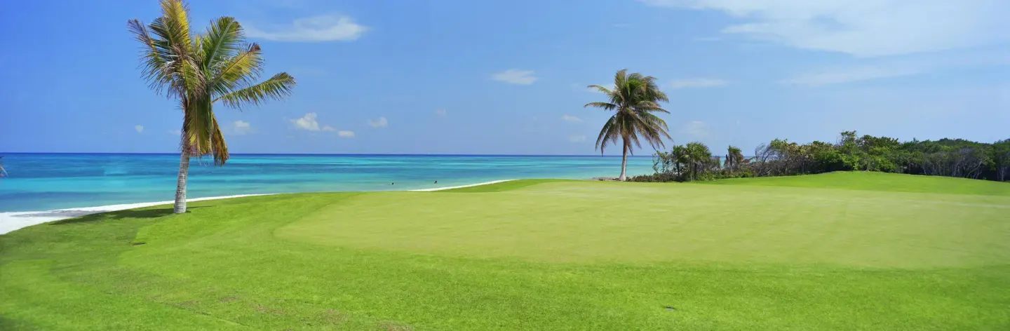 Seaside golf green with palm trees and blue ocean at Fairmont Mayakoba.
