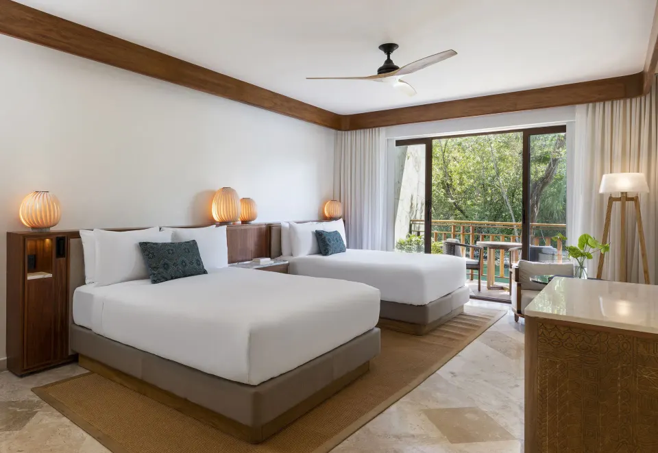 Two queen beds in a Casita Signature Room at Fairmont Mayakoba with a balcony facing trees.