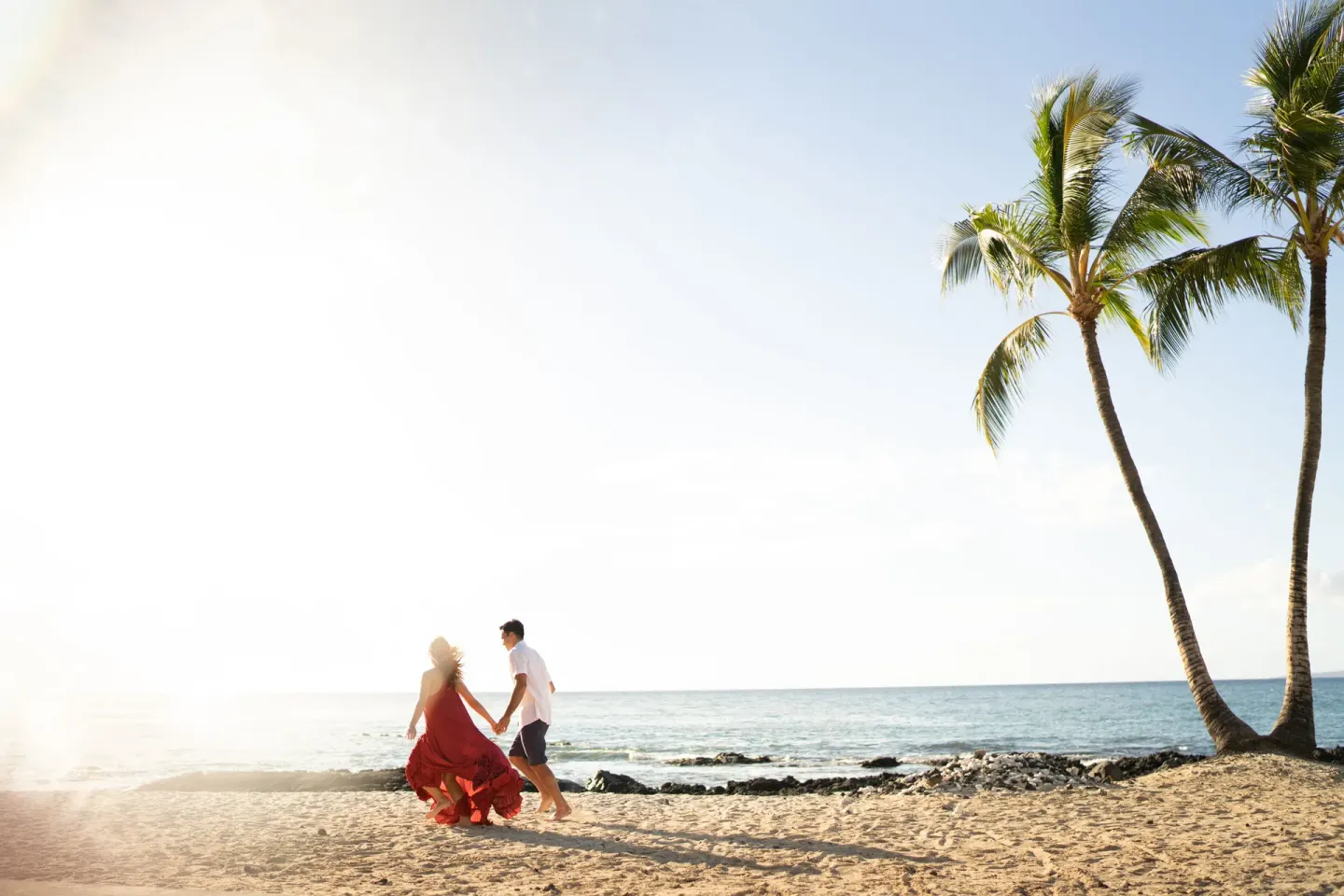 Couple walking on the beach at Fairmont Orchid with palm trees and ocean at sunset.