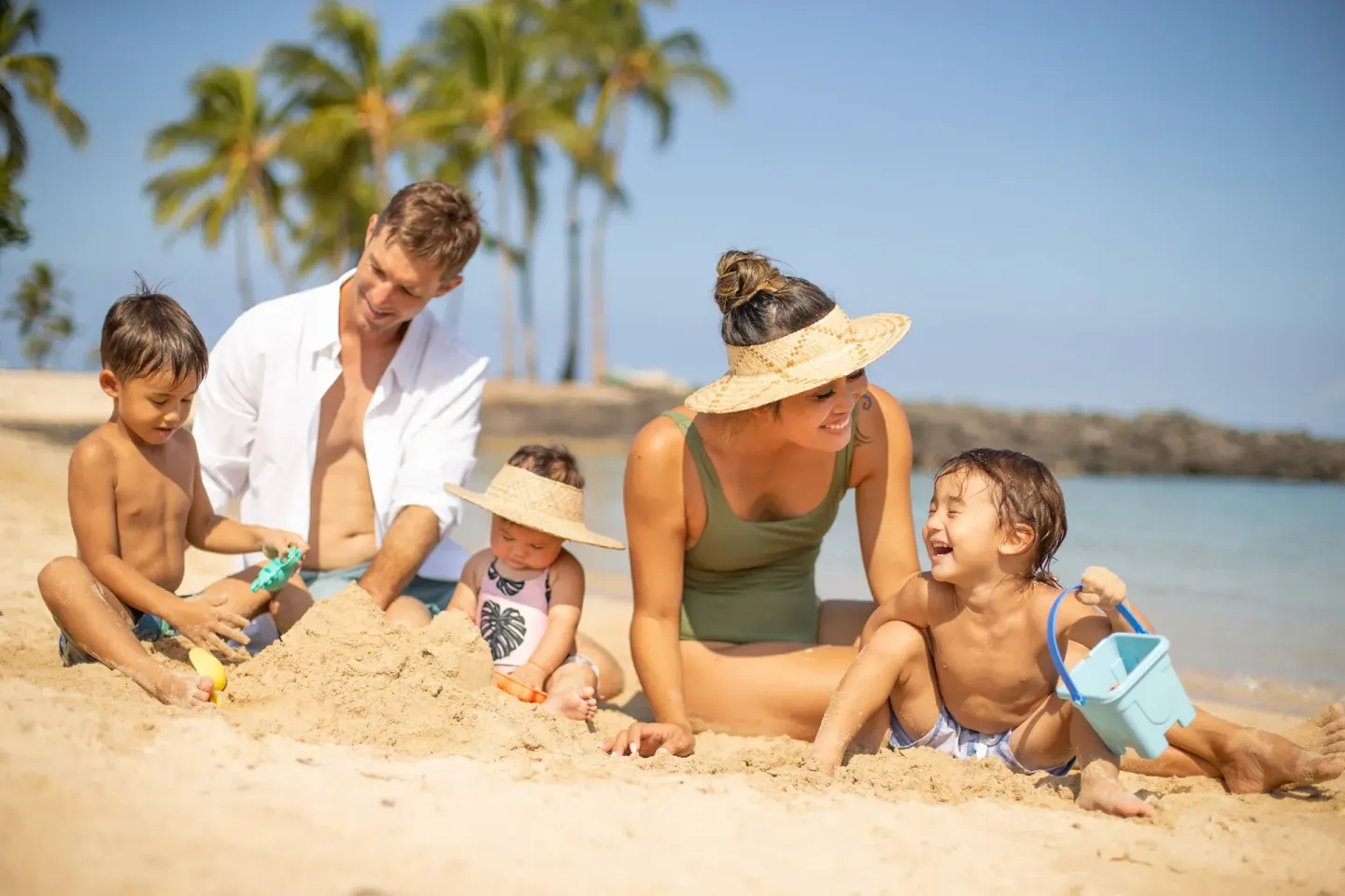 A family plays in the sand beside the water at Fairmont Orchid.