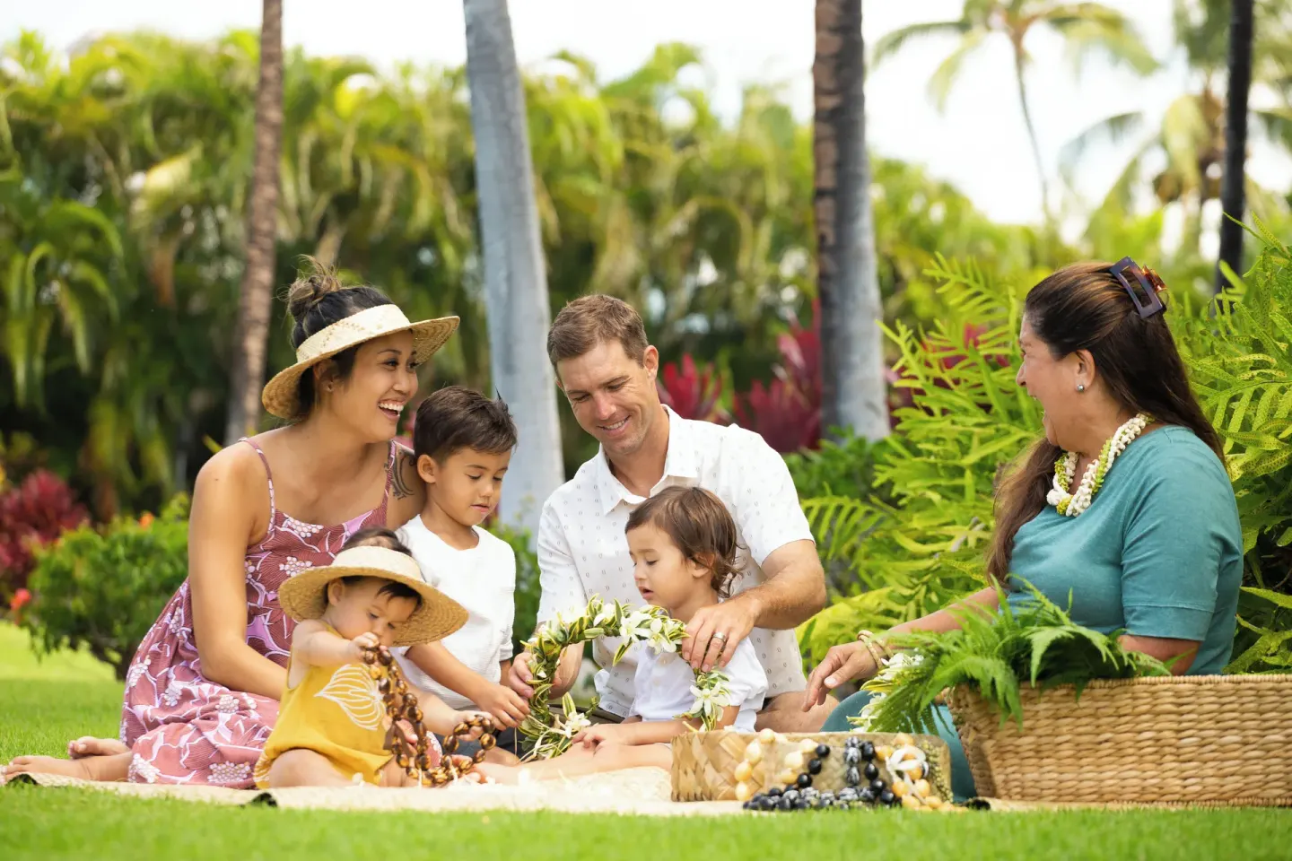 A family sits on the lawn making flower leis at Fairmont Orchid.