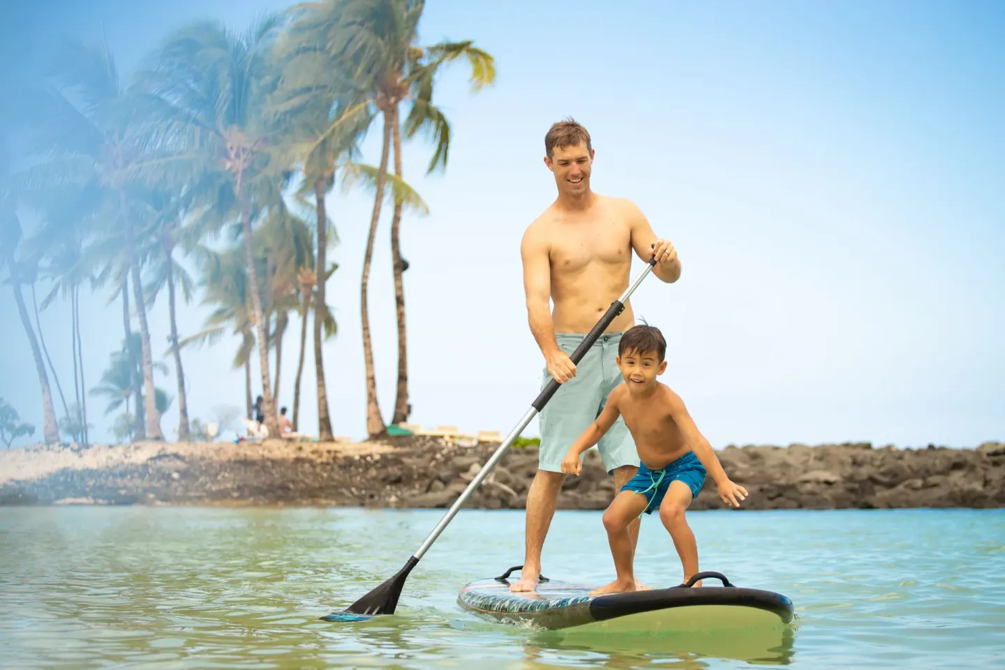 An adult and child stand on a paddleboard in calm water at Fairmont Orchid.
