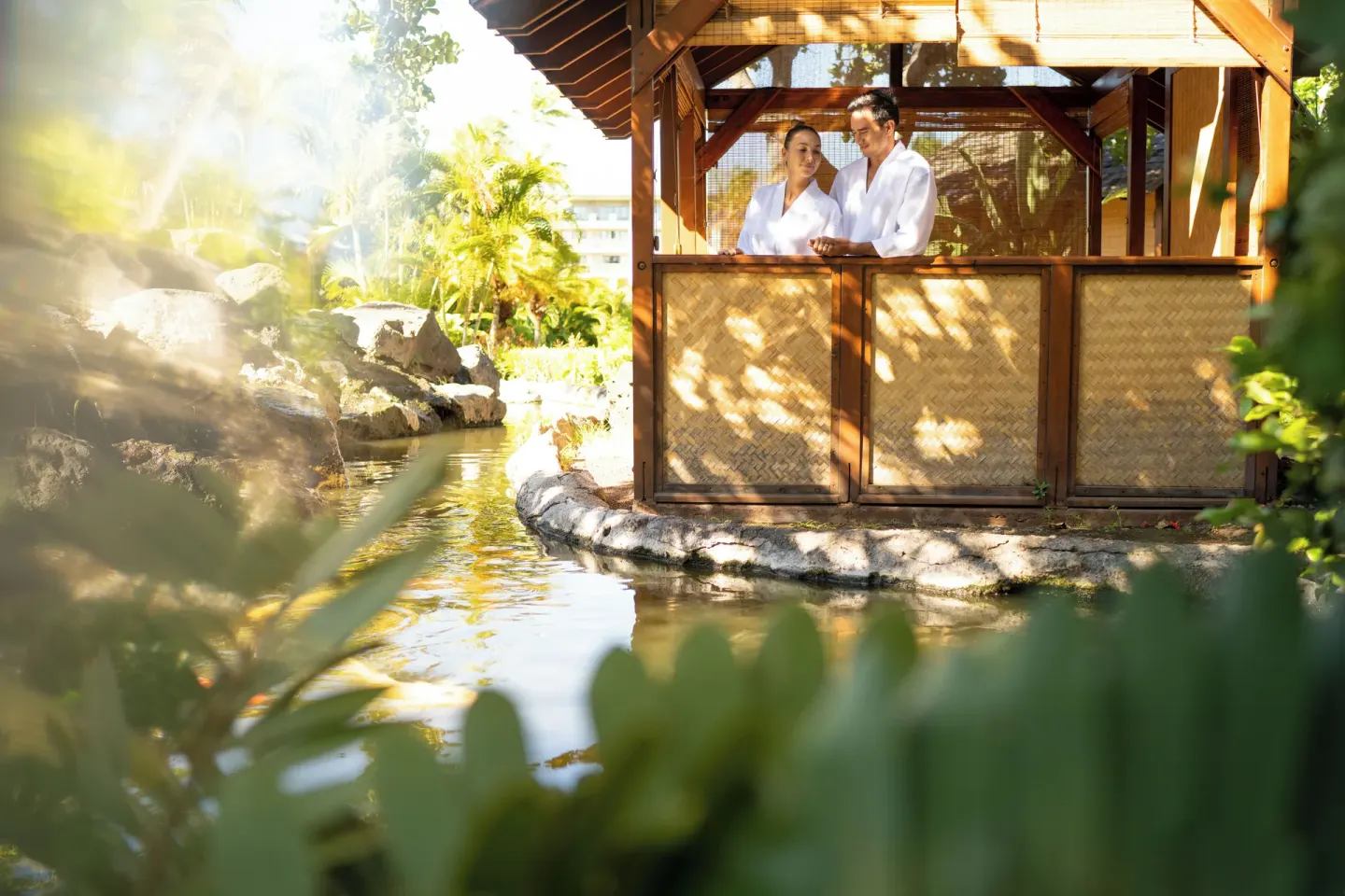 Guests in robes stand in a garden spa cabana beside water at Fairmont Orchid.