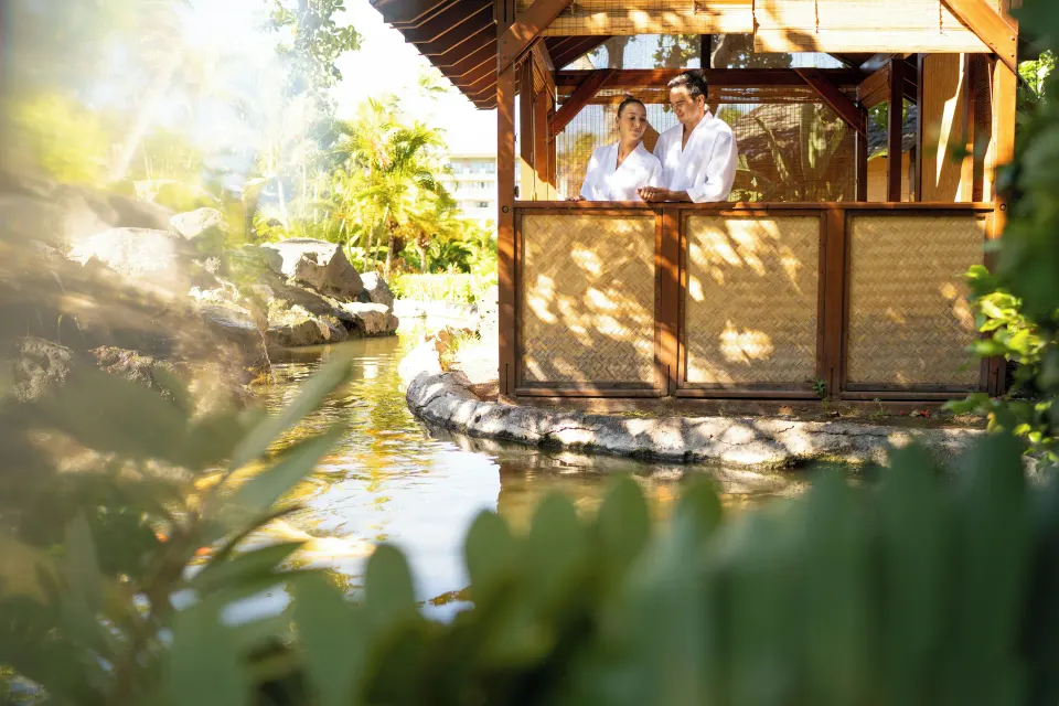 Guests in robes stand in a garden spa cabana beside water at Fairmont Orchid.