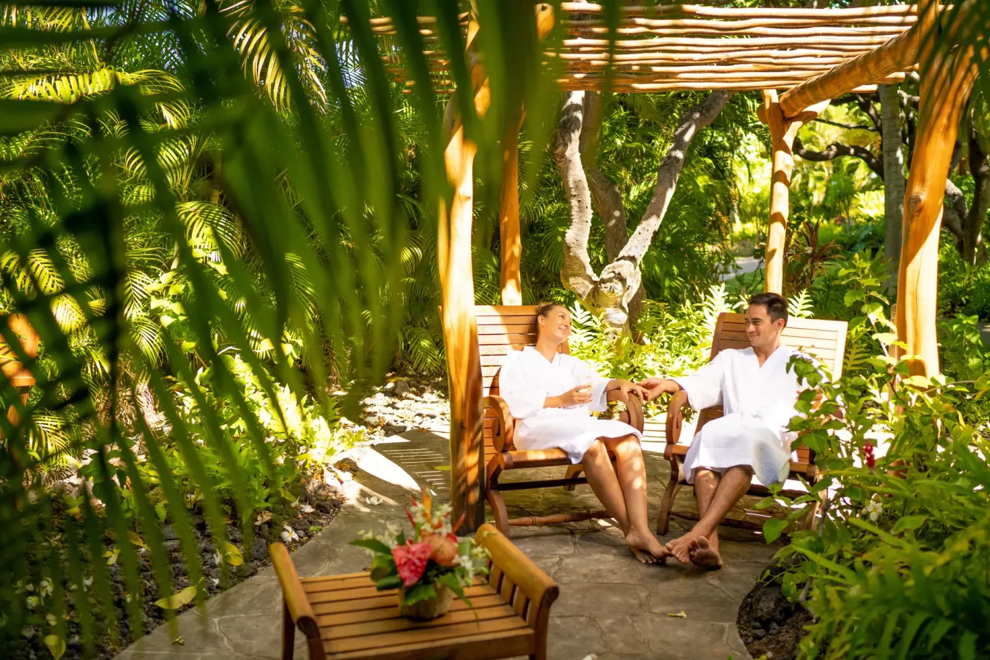 Guests in robes sit beneath a garden pergola at Fairmont Orchid.