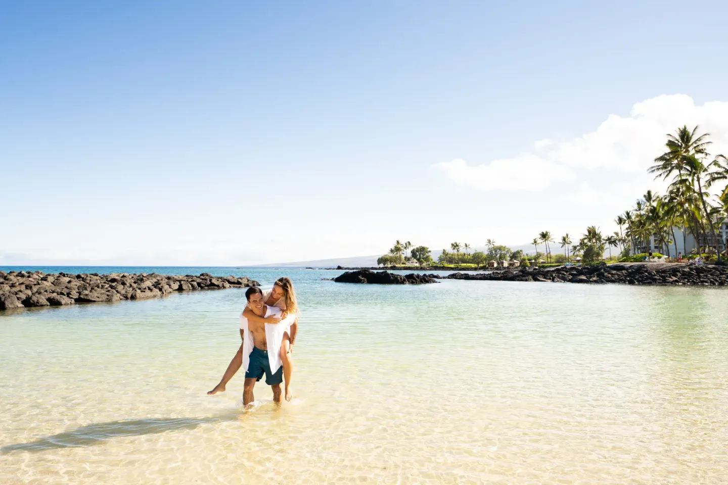Couple standing in clear lagoon water with palms and lava rock at Fairmont Orchid.