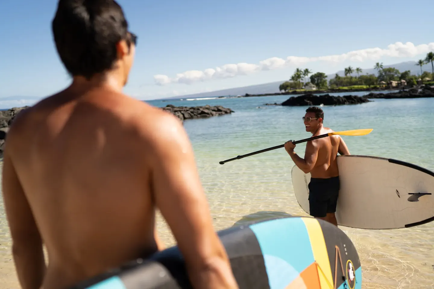 Two guests carry paddleboards into the ocean at Fairmont Orchid.