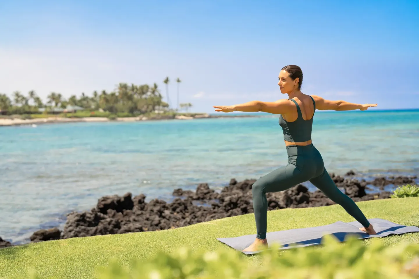 A yoga participant poses on a lawn beside the ocean at Fairmont Orchid.