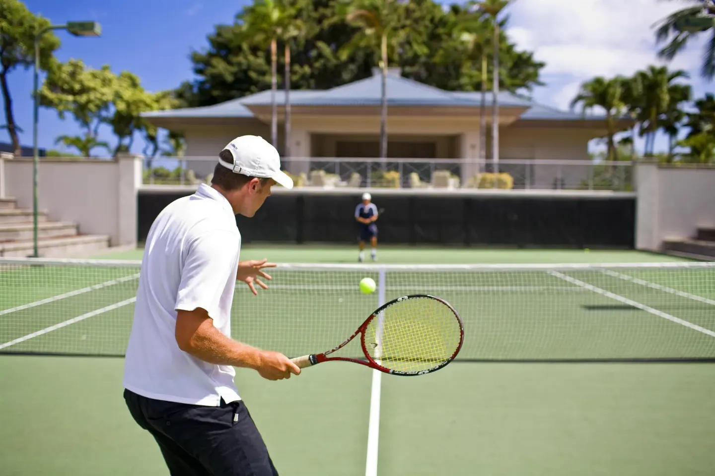 Two players rally on an outdoor tennis court at Fairmont Orchid.