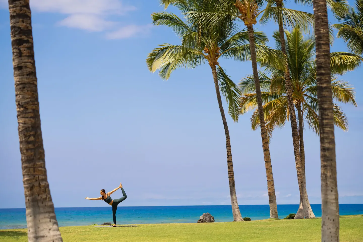 A yoga participant poses on an oceanfront lawn with palms at Fairmont Orchid.