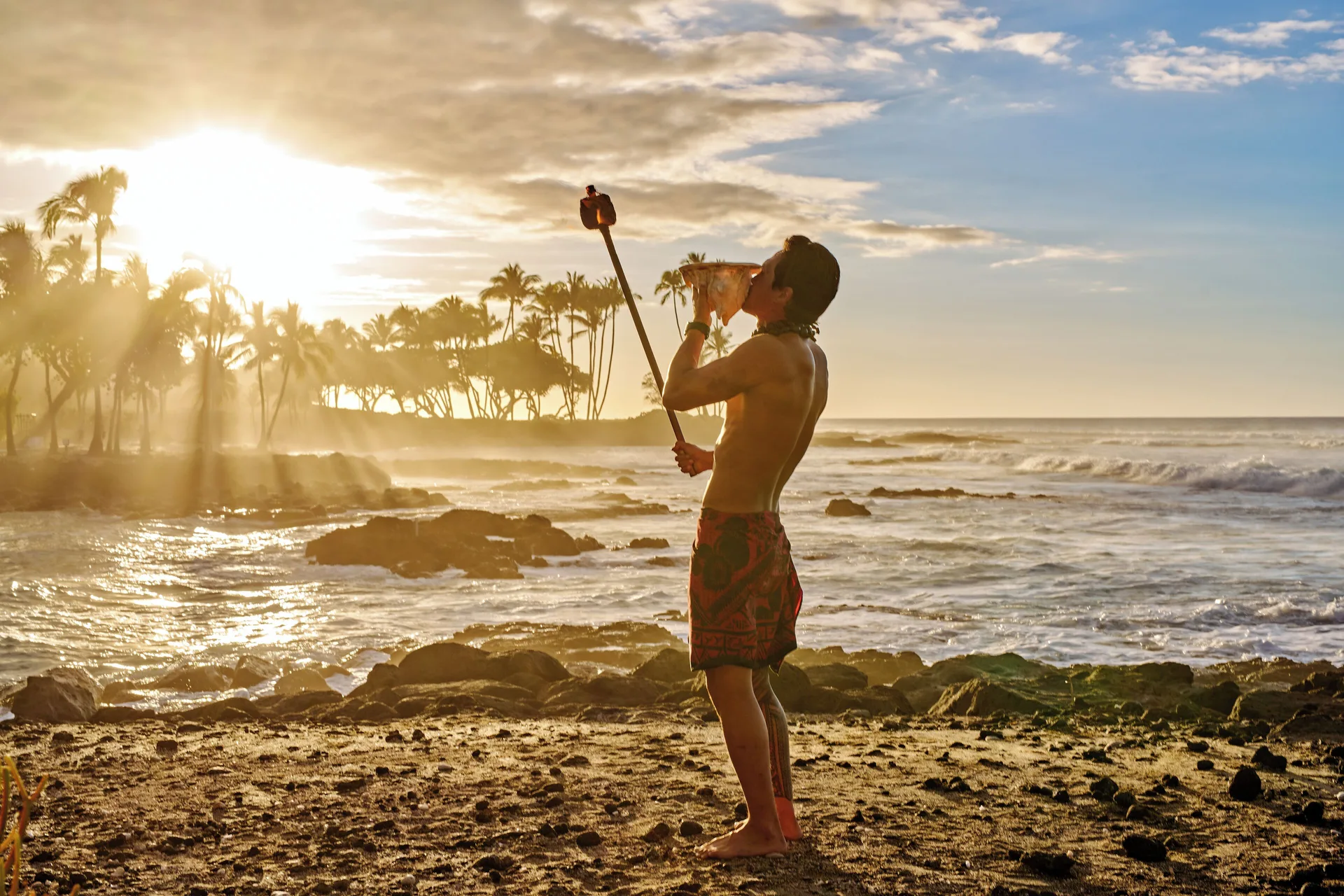 Man holding a torch on the rocky beach at sunset at Fairmont Orchid.