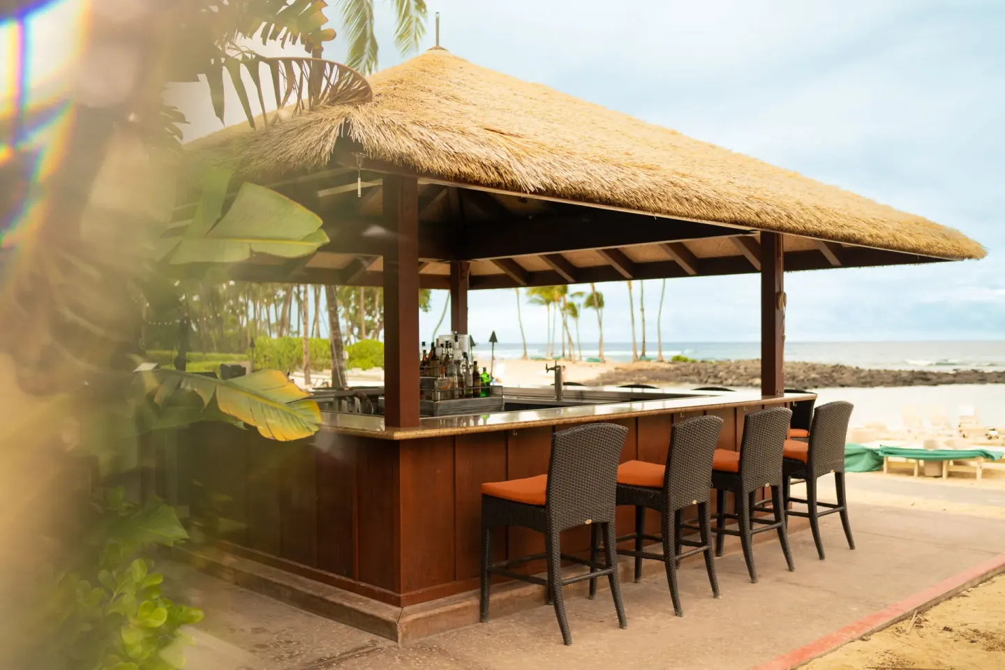 Thatched beachfront bar with stools beside the sand and ocean at Fairmont Orchid.