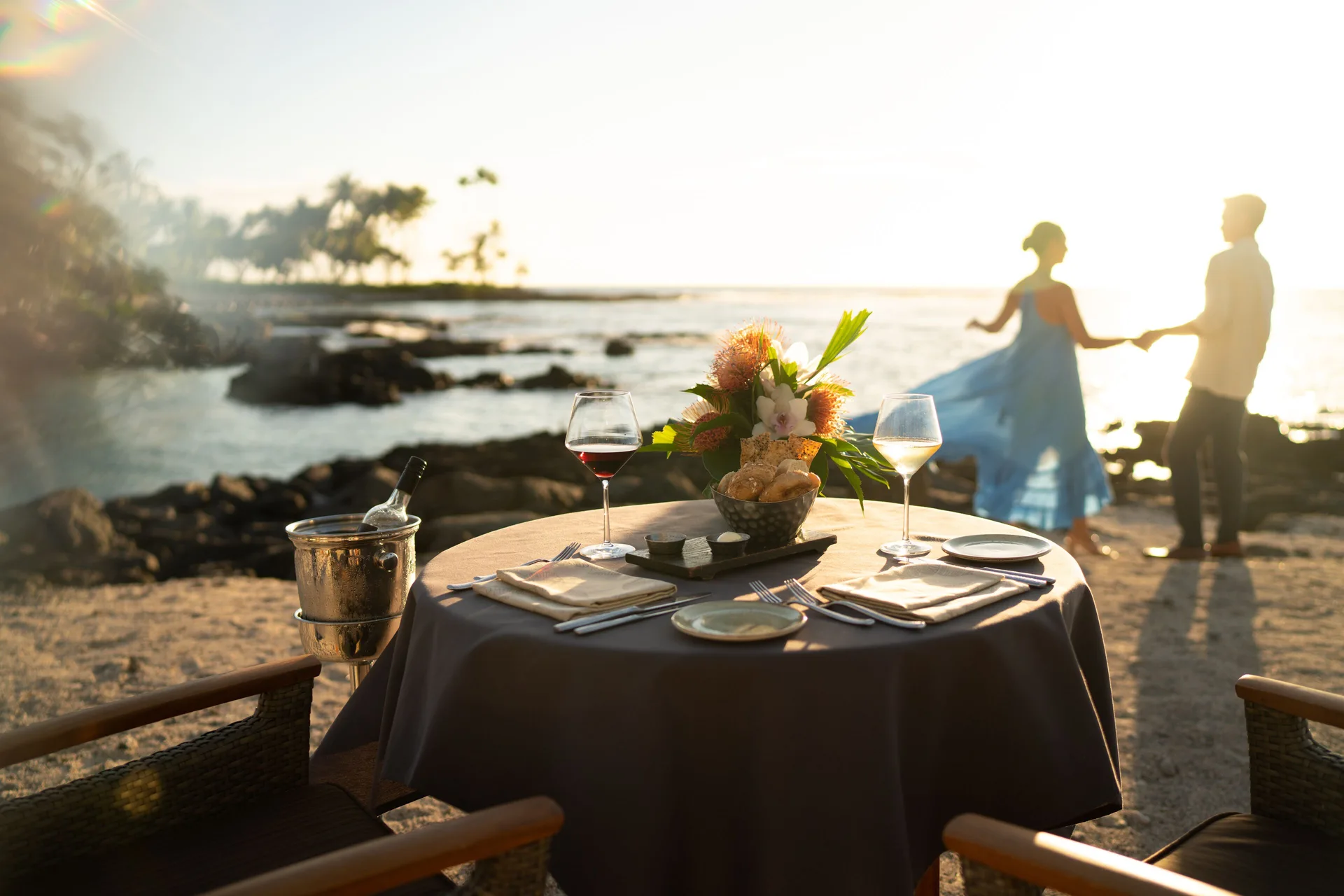 Beachside table for two with wine, flowers, and ocean sunset at Fairmont Orchid.