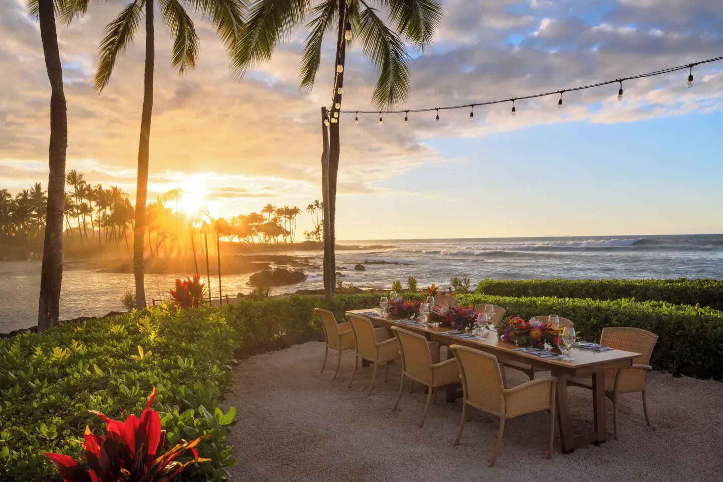 Oceanfront dinner table under palms and string lights at sunset at Fairmont Orchid.