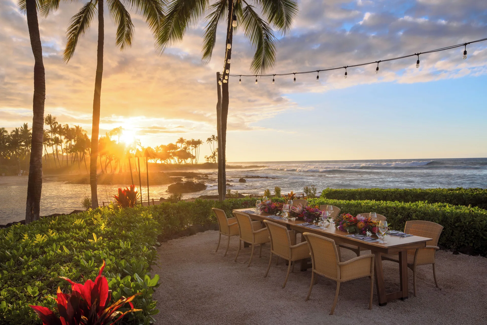 Oceanfront dinner table under palms and string lights at sunset at Fairmont Orchid.