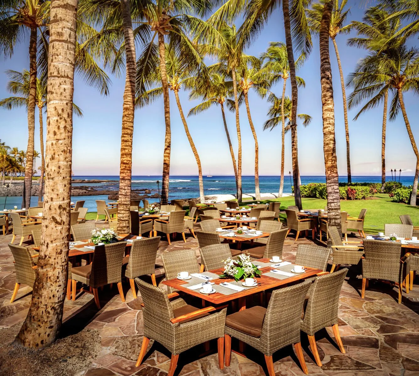 Outdoor oceanfront dining tables sit under palm trees at Fairmont Orchid.