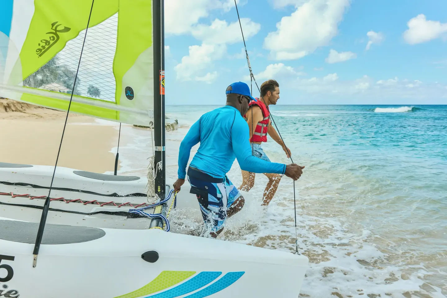 A guest and instructor launch a small sailboat from the beach at Fairmont Royal Pavilion.