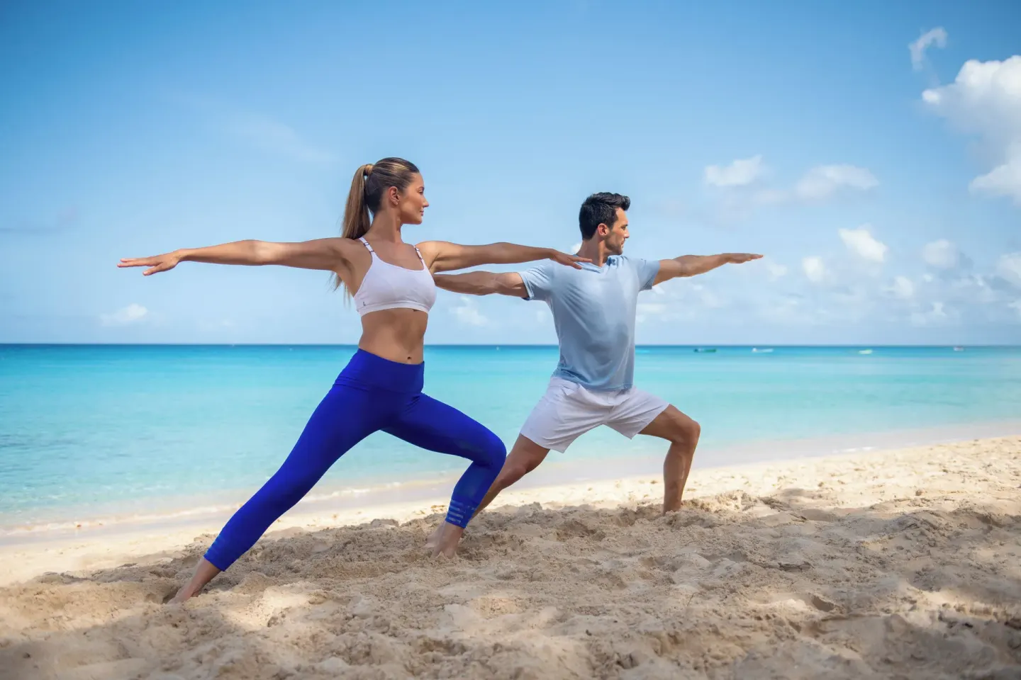 Two people practice yoga on the beach at Fairmont Royal Pavilion.