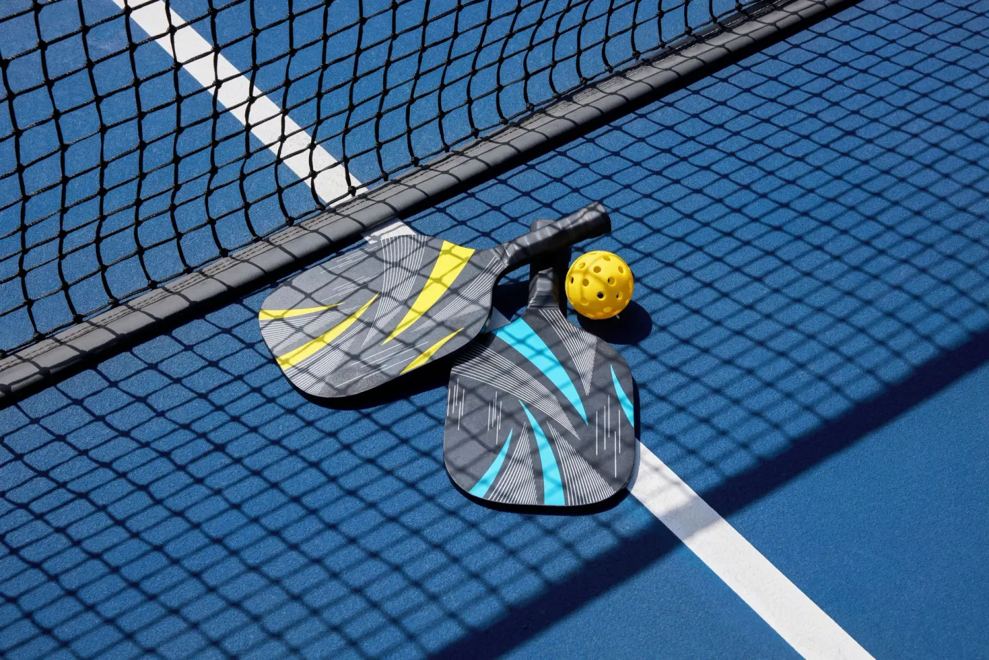 Pickleball paddles and ball on a blue court at Fairmont Royal Pavilion.